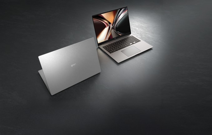 어두운 배경의 질감 있는 바닥 위로 세련된 실버 컬러의 LG 그램 노트북 두 대가 공중에 떠 있는 듯 입체적으로 배치되어 있으며, 한 대는 화면을 펼친 정면을, 다른 한 대는 슬림한 뒷면을 보여주는 이미지